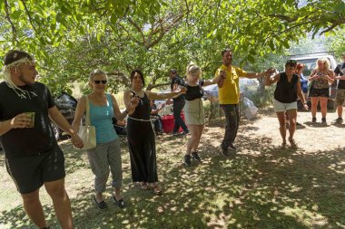 Girit, Yunanistan. Haziran 2019. Giritliler ve misafirleri sıcak bir yaz gününde Zeytin ağaçlarının gölgesinde dans ediyor..