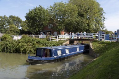 Devizes, Wiltshire, İngiltere, İngiltere. Ağustos 2019. Bir kafe binasının yanında Devies'teki Kennet & Avon Kanalı'nda bir kilitten çıkan mavi beyaz dar tekne.