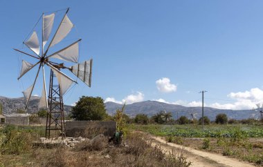 Lasithi Platosu, Doğu Girit, Yunanistan. Eylül 2019. Yel değirmeni sulama için bu manzaralı yerde su pompalıyor. Dağların Dikti aralığıyla çevrili..