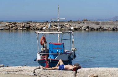 Gouves, Girit, Yunanistan. Ekim 2019. Balıkçı, Kato 'daki küçük limanda teknesinin yanında şekerleme yapıyor. Eski bir Amerikan askeri üssü.