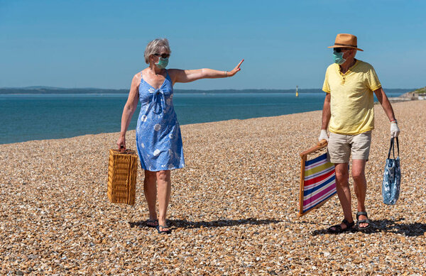 Southsea, Portsmouth, Southern England, UK. May 2020. Woman  wearing a surgical mask  social distancing from her husband during the Corvid-19 outbreak. On the beach in Southsea, UK.