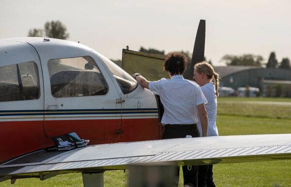 Gloucestershire, England, UK. 2020. A student about to take a flying lesson with her instructor from an English airfield. Instructor and student pilot check the engine.