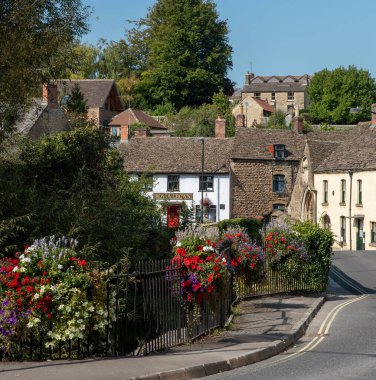  Malmesbury, Wiltshire, İngiltere, İngiltere. 2020 yılı. St Johns Köprüsü 'nün üzerindeki çiçek süslemesi bu kasabanın alt kısmında kırmızı kapılı bir bara doğru bakıyor..