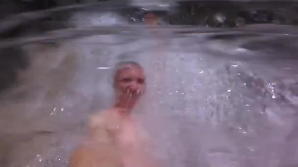 Een man staat onder een waterval. Water stroomt op hem. — Stockvideo
