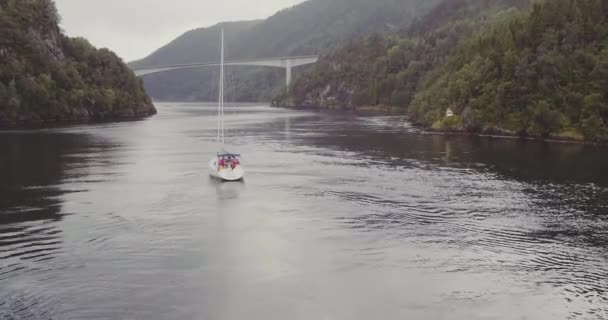 Яхты плывут вдоль фьорда между холмистыми побережьями к мосту — стоковое видео