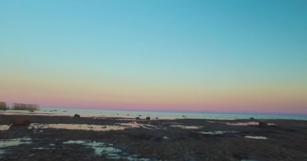 Luchtfoto beweging van besneeuwde grond tot uitgestrekte zee onder avondrood — Stockvideo