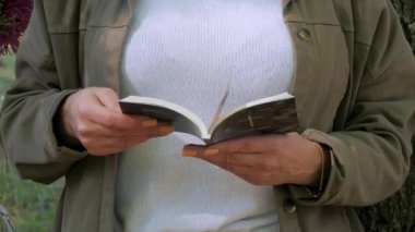 Dışarıda duran bir kadın elinde tutarken küçük bir kitap okuyor.