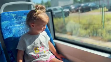 Küçük kız mutlu bir şekilde tramvaya biniyor ve merakla pencereden dışarı bakıyor. Seyahat ve keşif atmosferi