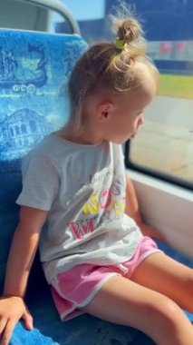 Küçük kız hayranlıkla tramvaya biniyor, neşe ve merakla pencereden dışarı bakıyor, gezinin ve manzaranın tadını çıkarıyor.