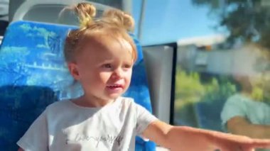 Küçük kız tramvayda gezmekten hoşlanıyor, pencereden merakla bakıyor. Neşe atmosferi, çocukluk ve kentsel hareket