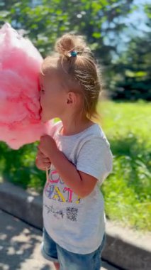 Küçük kız elinde pamuk şeker tutuyor ve aile yürüyüşünün tadını çıkarıyor. Çocukluk sevincinin, sevginin ve mutlu anların sembolü.