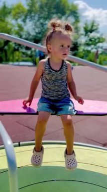 Renkli bir oyun parkında oturan küçük kız güneşli bir günde dönüyor ve eğleniyor. Neşeli ve tasasız çocukluk atmosferi