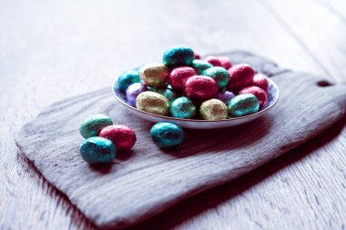 Ahşap kesme tahtasıüzerine yerleştirilen renkli folyoya sarılmış Paskalya yumurtası tabağı