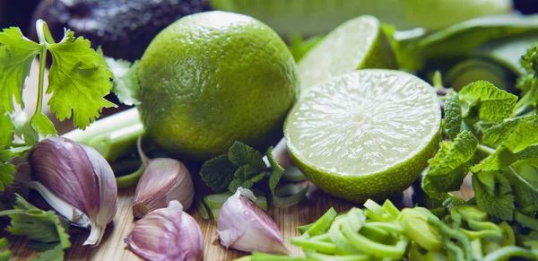 chopped limes with greens and garlic cloves on wooden board