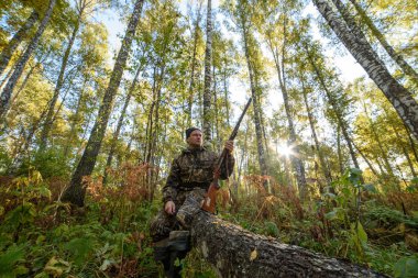 Avcı sarı yapraklar ağaçlarıyla çerçevede bir sonbahar ormandaki bir silahla
