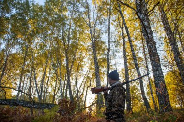 Avcı sarı yapraklar ağaçlarıyla çerçevede bir sonbahar ormandaki bir silahla