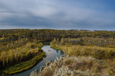 Dolambaçlı bir nehir vadi boyunca akar. Bulutlu gökyüzü ve sonbahar yaprakları renk.