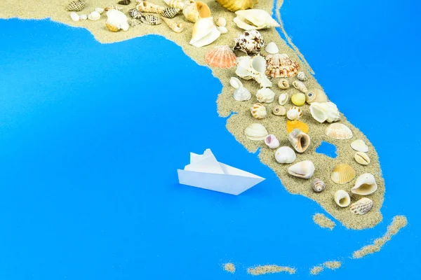 A paper boat stands off the coast of Florida. The contours of Florida lined with sand, on top - shells.