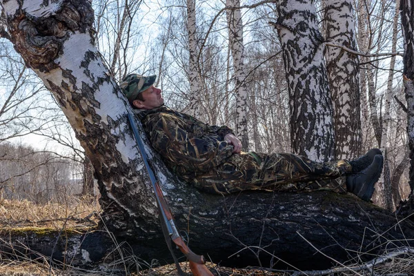 The hunter with a gun stopped to rest on a tree trunk.