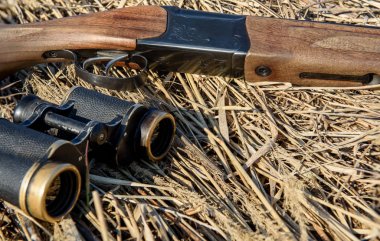 Dürbün ve av tüfeği kuru otların üzerinde yatıyor. Avcı mühimmatı.