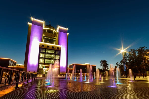 The building of the Novosibirsk University at night with illumination, a multi-colored fountain.