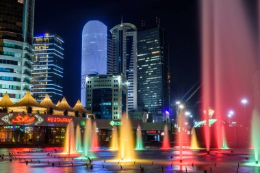 Nur-Sultan, Kazakistan, Ağustos 2019, Kazakistan'ın başkentinin merkezinde ki yüksek binaların arka planında aydınlatmalı çeşmeler.