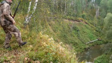 Bir silah ile bir avcı sonbahar ormanda oyun izler.