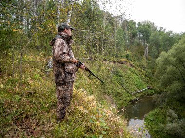 Bir silah ile bir avcı sonbahar ormanda oyun izler.