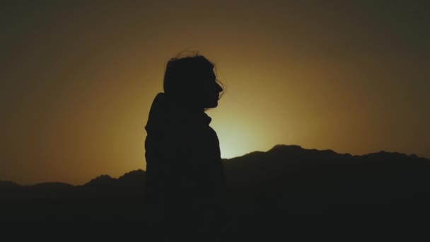 Gün batımında çölde yürüyen güzel genç bir kadının silueti. Çölde giden bir kadın, kum tepeleri, rüzgar esintisi, 4K — Stok video