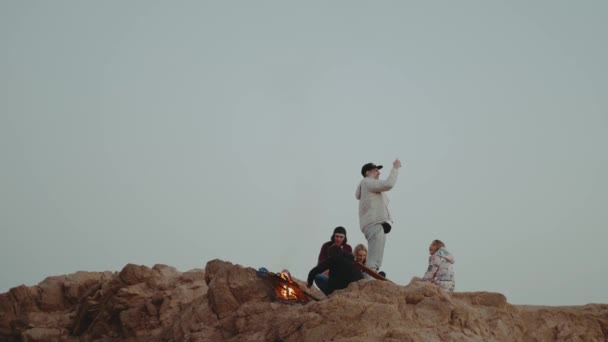 Grupa ludzi relaksujących się na szczycie góry na zachodzie słońca, siedzących przy ognisku, cieszących się czasem - przyjaźń, młodzież, 4k — Wideo stockowe