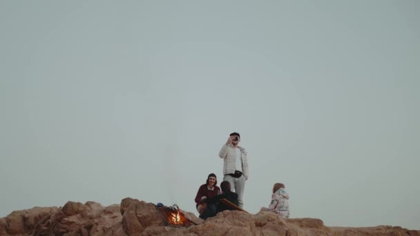 Grupo de personas que se relajan en la cima de una montaña al atardecer, sentados cerca de la hoguera, disfrutando de su tiempo - amistad, juventud, 4k — Vídeos de Stock