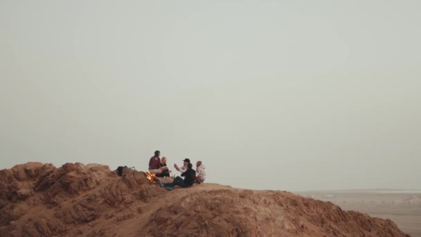 Grupo de personas que se relajan en la cima de una montaña al atardecer, sentados cerca de la hoguera, disfrutando de su tiempo - amistad, juventud, 4k — Vídeo de stock