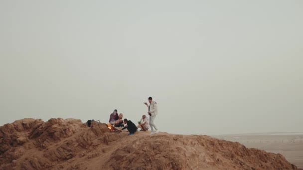 Grupo de personas que se relajan en la cima de una montaña al atardecer, sentados cerca de la hoguera, disfrutando de su tiempo - amistad, juventud, 4k — Vídeo de stock