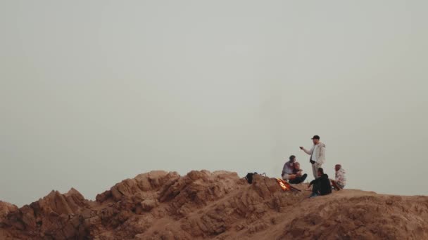 Skupina lidí relaxuje na vrcholu hory při západu slunce, sedí blízko táboráku, užívají si svůj čas - přátelství, mládež, 4k — Stock video