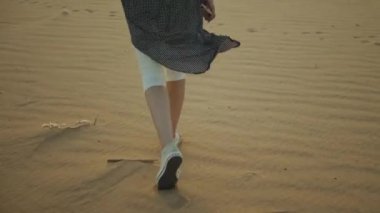 Güzel sarışın kadın çölde gün batımında yürüyor. Çölde giden kadın, kum tepeleri, yakın çekim, yavaş çekim, 4k