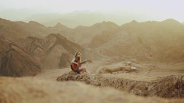 Gitar çalan ve çölde şarkı söyleyen kadın gün batımında manzara, çöl arka planı, 4k