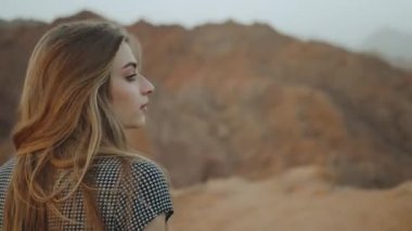 Uzun elbiseli genç sarışın kadın dağın tepesinde yürüyor. Gün batımlı dağ manzarası, 4k