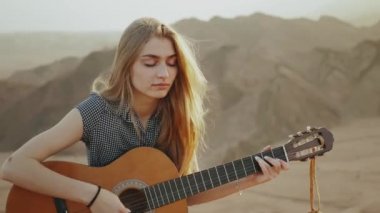 Gitar çalan ve çölde şarkı söyleyen kadın gün batımında manzara, çöl arka planı, 4k