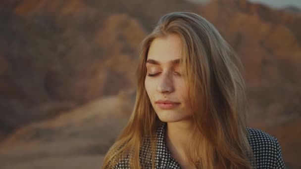 노을에 눈을 감고 있는 예쁜 금발 여자의 초상화. 사막 의산에서 있는 행복 한 젊은 여자, 일몰 광경 , 4k — 비디오