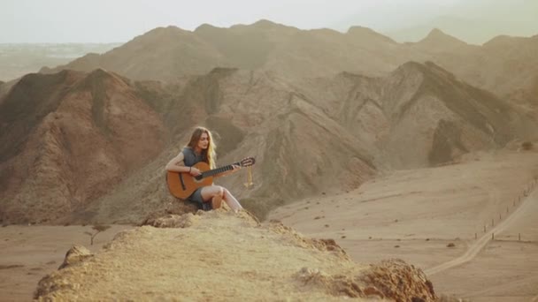 Žena hraje na kytaru a zpívá v poušti v západu slunce krajiny, pouštní hory pozadí, 4k — Stock video
