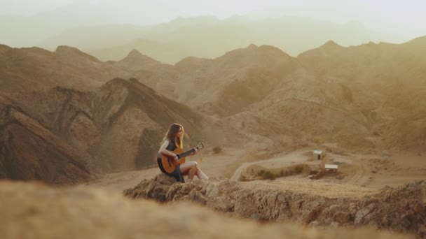 Mulher tocando guitarra e cantando no deserto em paisagens do pôr do sol, deserto montanhas fundo, 4k — Vídeo de Stock