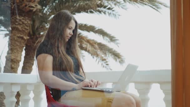 Dizüstü bilgisayarda çalışan güzel bir kız öğrenci ya da serbest çalışan bir kadın, balkonda oturan, avuç içi ve deniz manzaralı bir kadın, 4K — Stok video