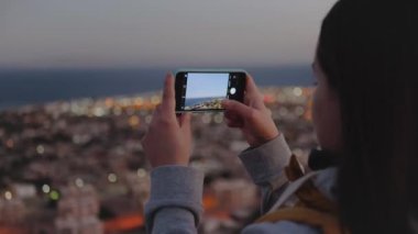 Akşamları kadın akıllı telefondan denizin fotoğrafını çeker. Kadın dağın tepesinde kal ve Horizon 'a bak, 4k