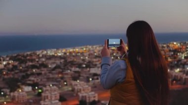 Akşamları kadın akıllı telefondan denizin fotoğrafını çeker. Kadın dağın tepesinde kal ve Horizon 'a bak, 4k