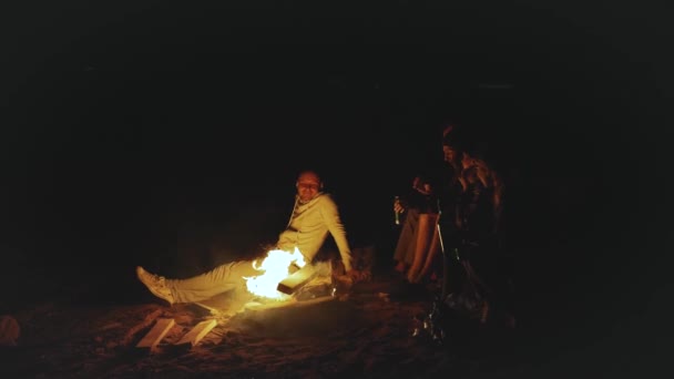 Skupina přátel baví v blízkosti táboráku na pláži u moře v noci, 4k — Stock video