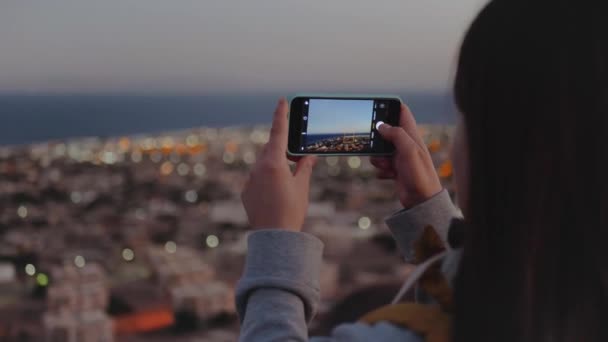 Mujer tomar una foto del mar por teléfono inteligente en la noche. Mujer permanecer en la cima de la montaña y mirando en Horizonte, 4k — Vídeo de stock