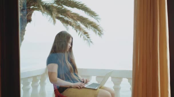Όμορφη γυναίκα φοιτητής ή ελεύθερος επαγγελματίας που εργάζονται σε ένα φορητό υπολογιστή, γυναίκα που κάθεται στο μπαλκόνι με την κορυφή παλάμη θέα και τη θάλασσα, 4k — Αρχείο Βίντεο