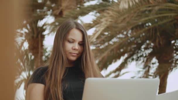 Krásná žena student nebo na volné noze pracující na notebooku, žena sedí na balkóně s horní pohled na dlaň a moře, 4k — Stock video