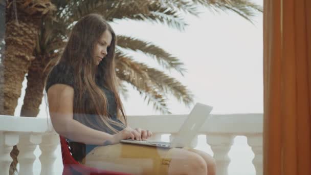 Bella studentessa o freelance che lavora su un computer portatile, donna seduta in balcone con vista dall'alto palmo e mare, 4k — Video Stock