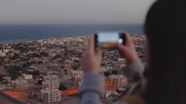 Akşamları kadın akıllı telefondan denizin fotoğrafını çeker. Kadın dağın tepesinde kal ve Horizon 'a bak, 4k